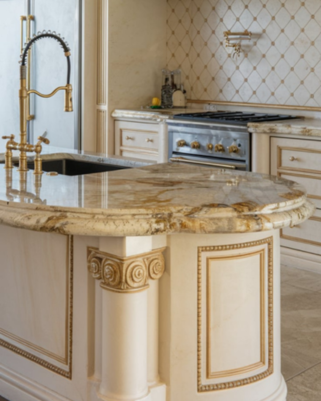 A photo of a luxury kitchen with a double ogee-edged granite countertop. The countertop has two stacked curves and a grand, elaborate design. There is a sink on the left, and a gold faucet with a curved spout. There are also a few appliances, such as a refrigerator, oven, and dishwasher. The backsplash has a unique pattern and is adorned with gold accents. The floor is made of tiles.
