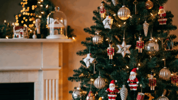 A Christmas tree decorated with various vintage ornaments including mercury glass baubles, pinecones, toy soldiers, retro Santas, tinsel ornaments, and handmade cloth pieces in a cozy holiday living room.