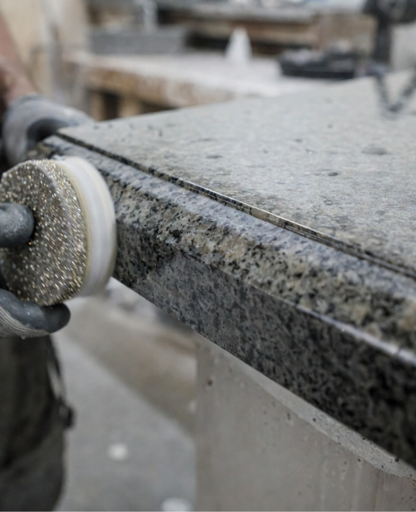 How to Make an Ogee Edge on Granite / Close-up of granite ogee edge being polished with a diamond polishing pad, wet surface, visible matte texture, worker wearing gloves, workshop environment, realistic stone surface details, macro photography style, high resolution